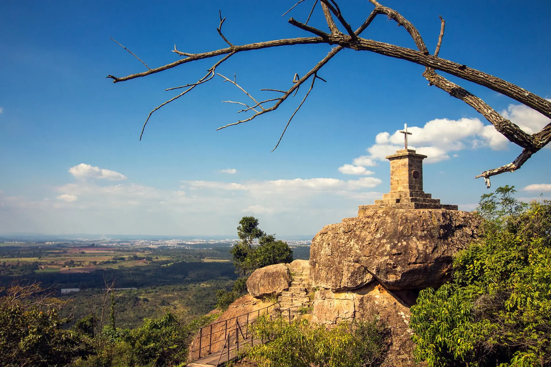 Monólito com capela no topo de um morro, com vista do horizonte sob céu azul